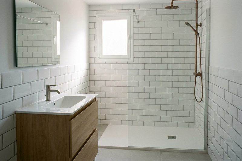 Cuarto de baño terminado con alicatado blanco, mueble de lavabo de madera clara, espejo rectangular y plato de ducha a ras de suelo